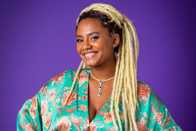 jéssica ellen posando sorridente em fundo roxo com blusa verde com detalhes coloridos